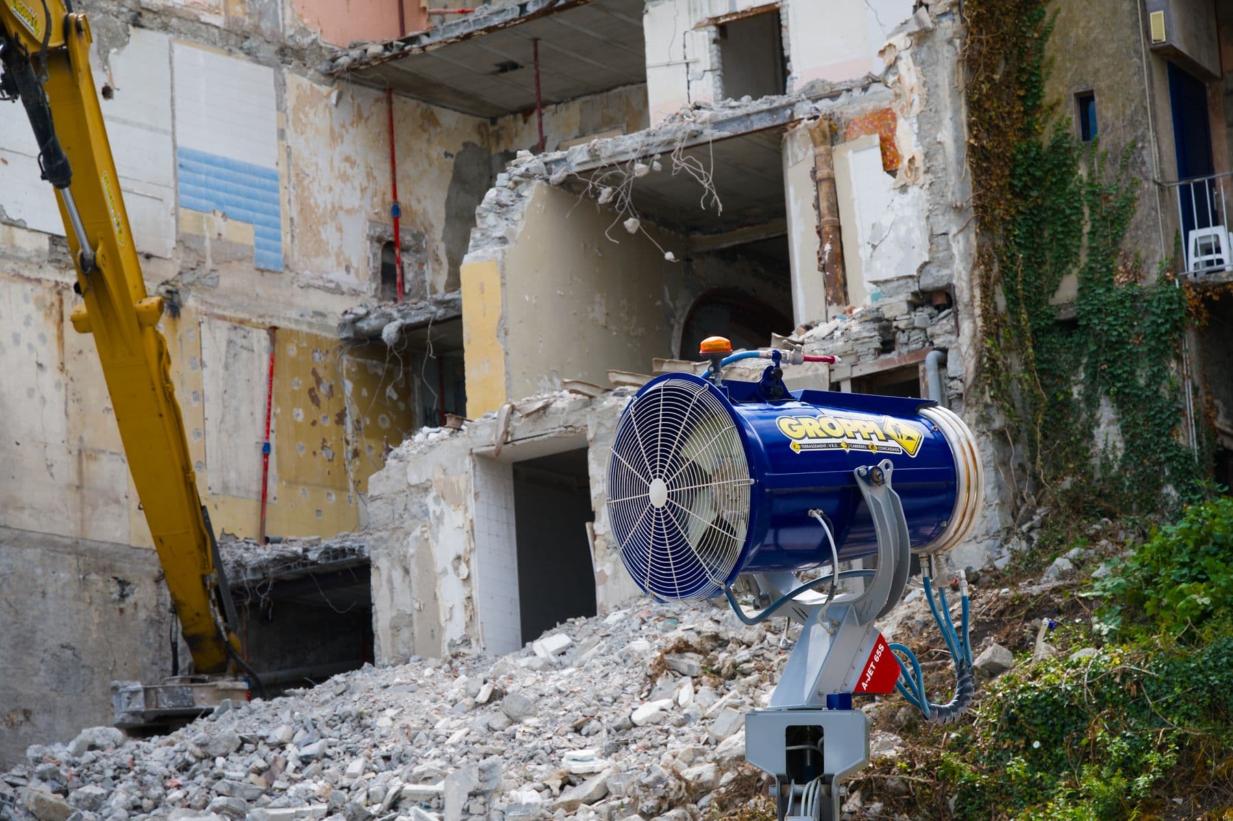 A dust-control fan aimed at a concrete building that is partly demolished.