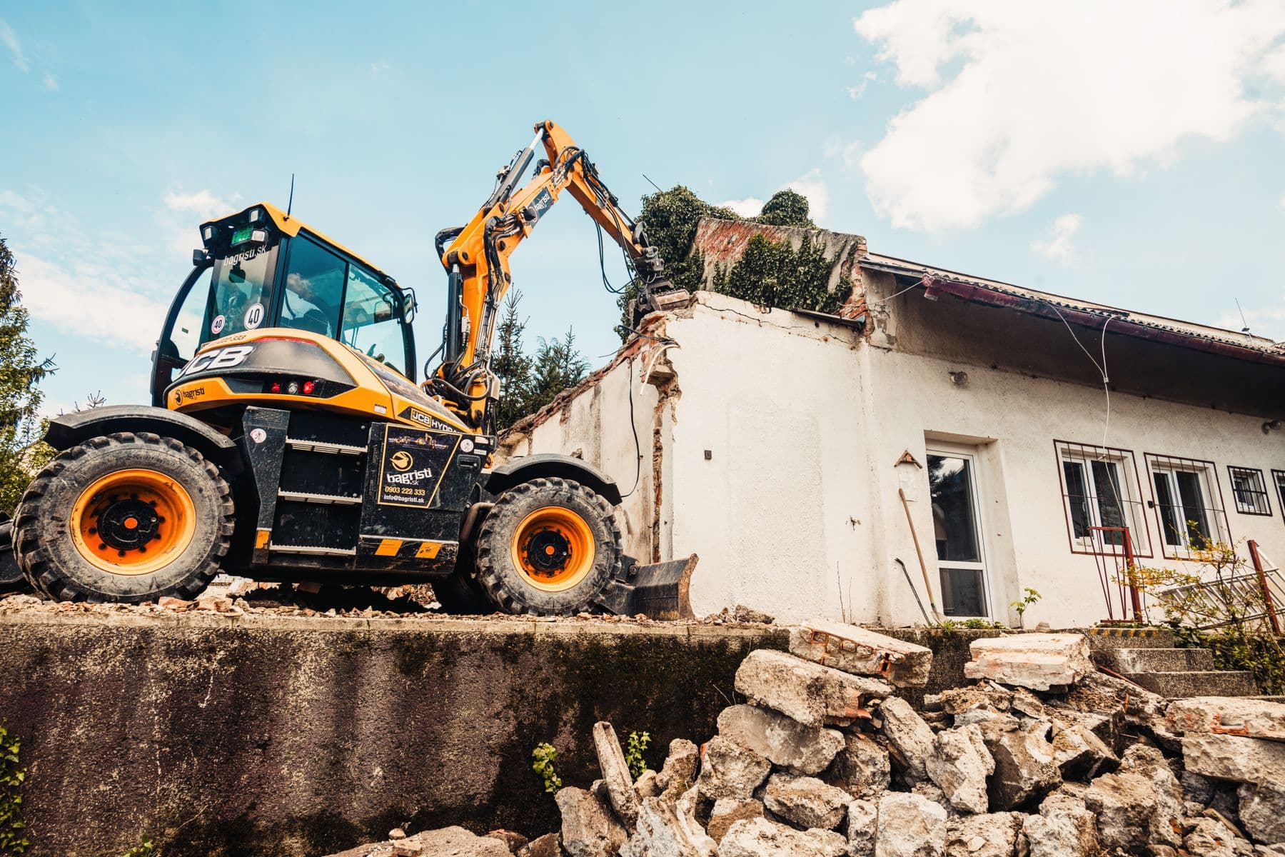 A small excavator and a loader working beside a low, single-story building.