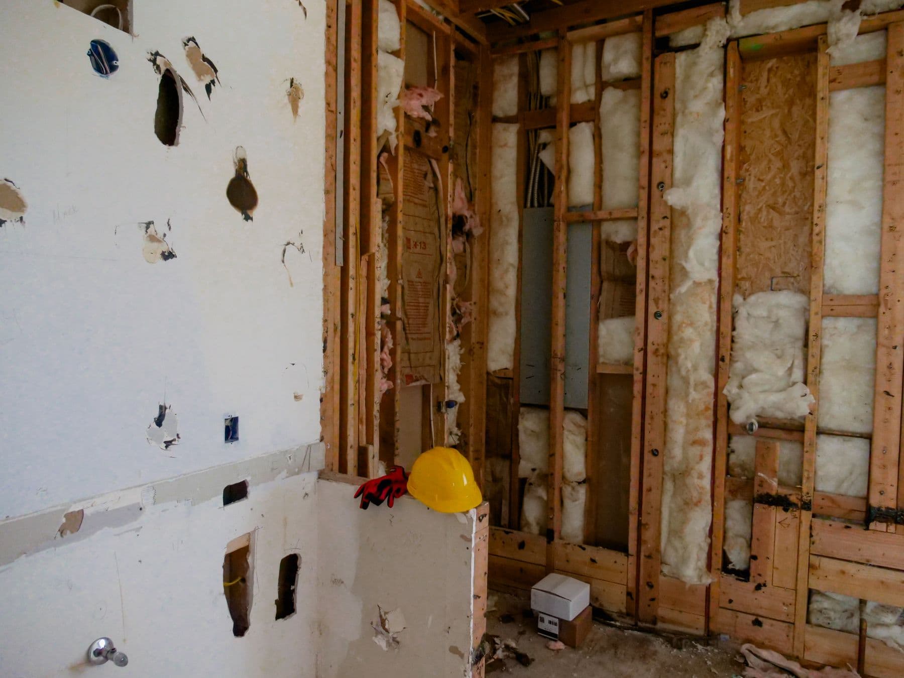 A room stripped back to its wood studs, with a hard hat resting on the framing.