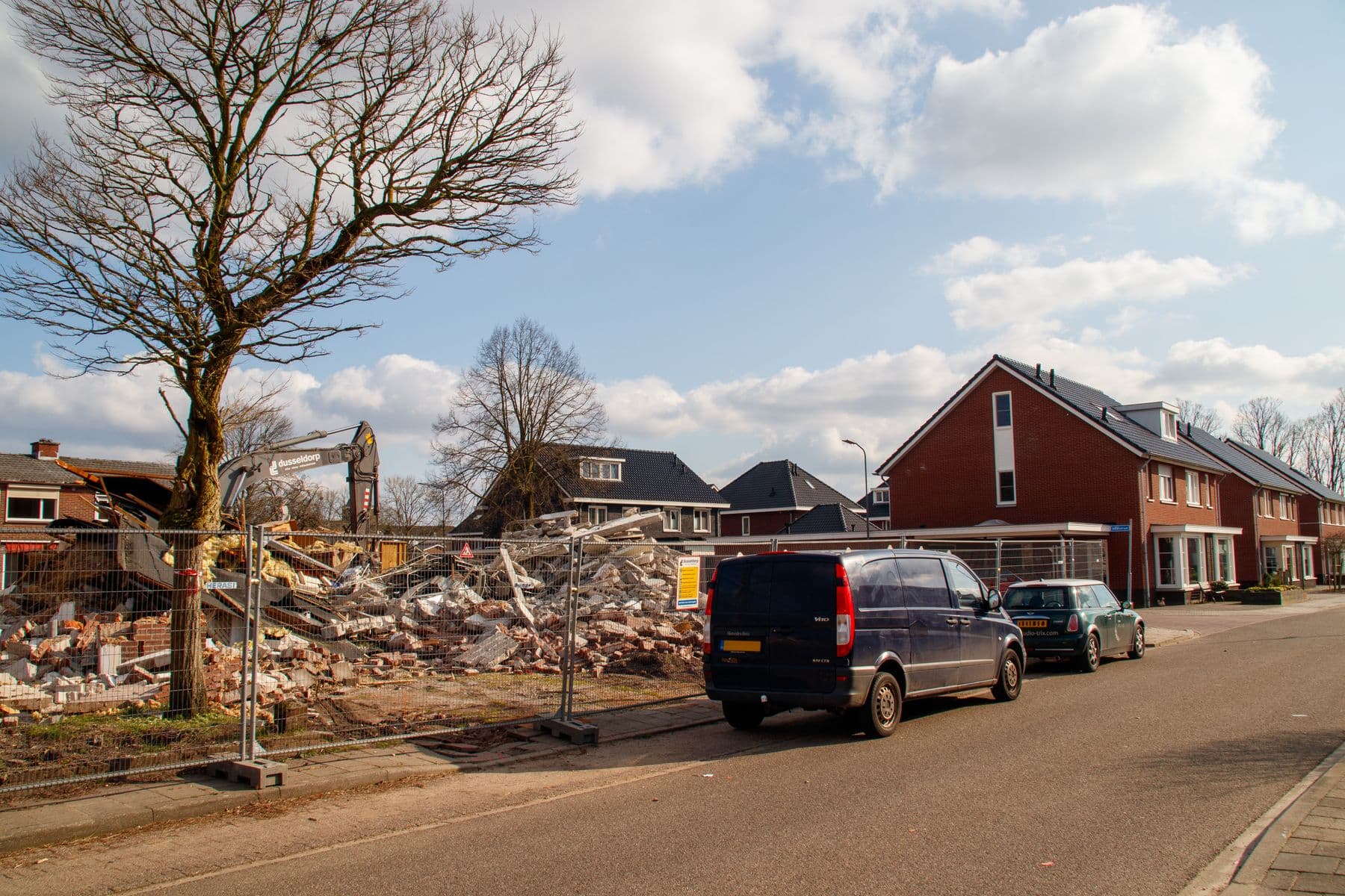 A demolished house reduced to rubble on a residential street, behind a site fence.